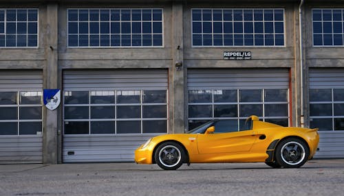 Free Yellow Coupe Parked Near Brown Painted Warehouse Stock Photo