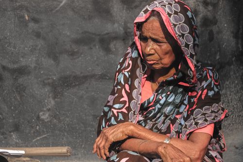 Free Portrait of an elderly South Asian woman wearing colorful traditional clothing seated outdoors in Dhaka. Stock Photo