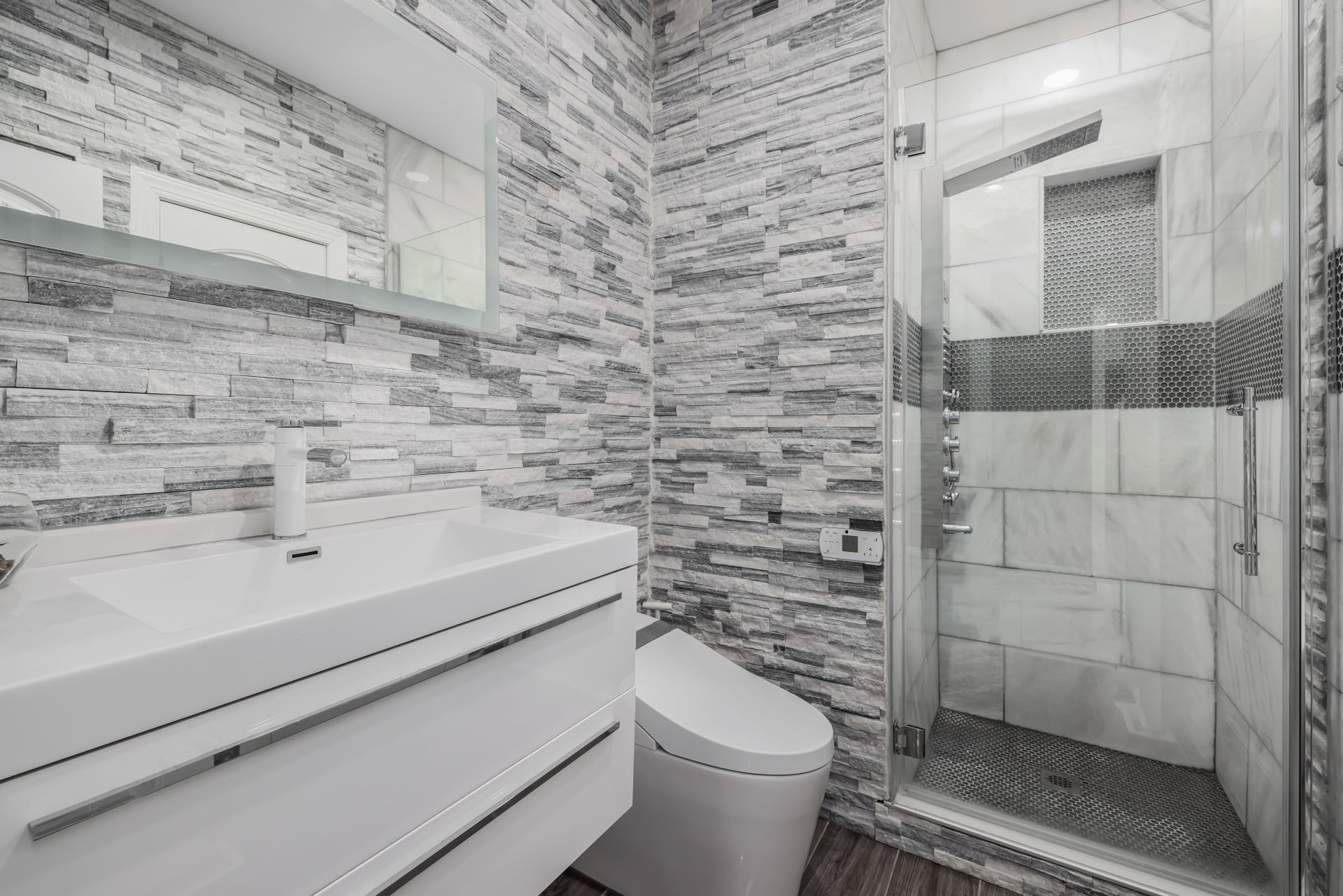 Stylish modern bathroom featuring a glass shower, stone walls, and sleek white vanity.