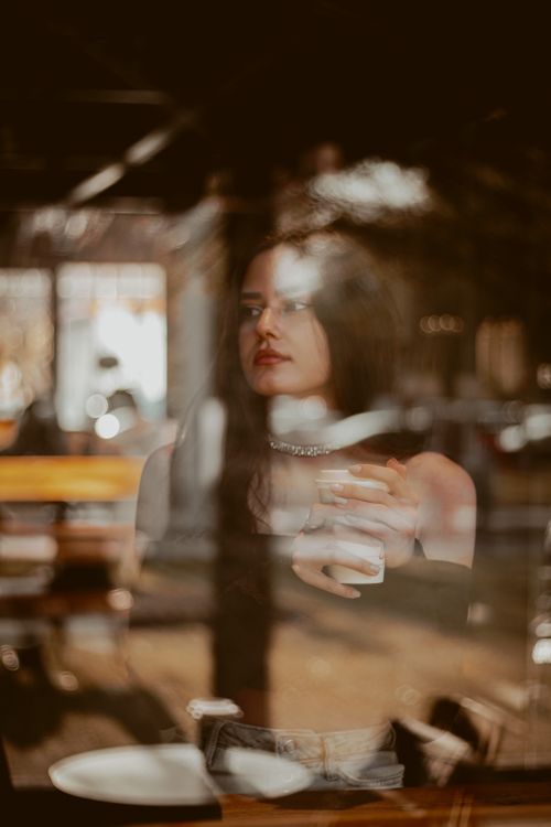 Free A serene moment captured of a woman holding coffee, reflected through cafe glass in Konya, Turkey. Stock Photo