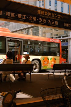 Urban bus featuring artwork next to passengers at a Japanese bus stop.