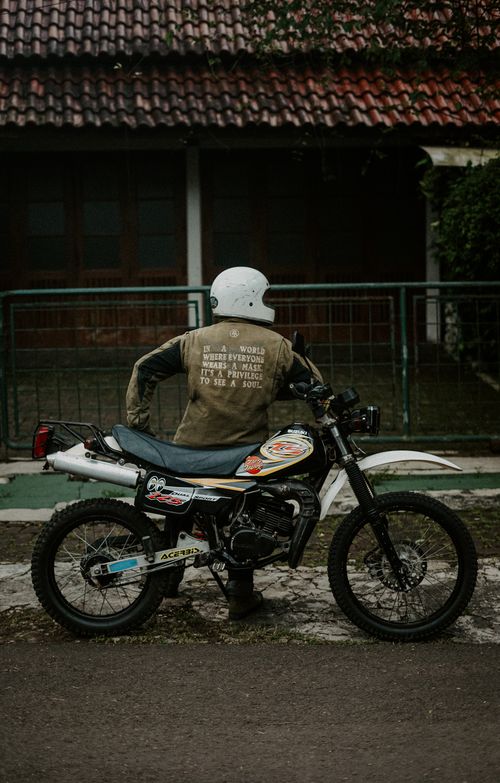 Free A motorcyclist in a helmet stands next to a parked bike outside a rustic building. Stock Photo
