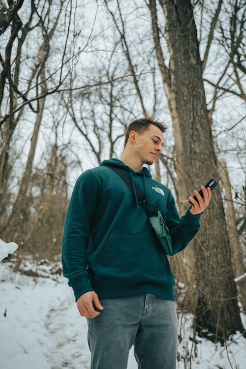 Free Man in Green Hoodie Sweater Holding Black Smartphone Stock Photo