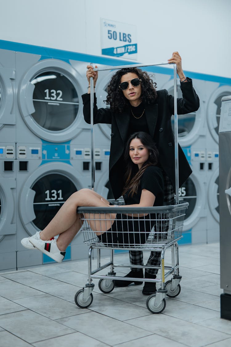 Woman Sitting In Cart And Man In Laundromat