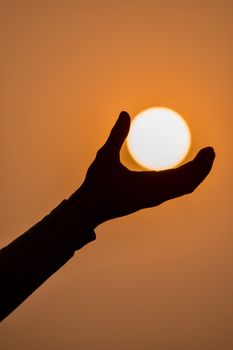 A silhouette of a hand reaching towards the setting sun, capturing a serene sunset moment.