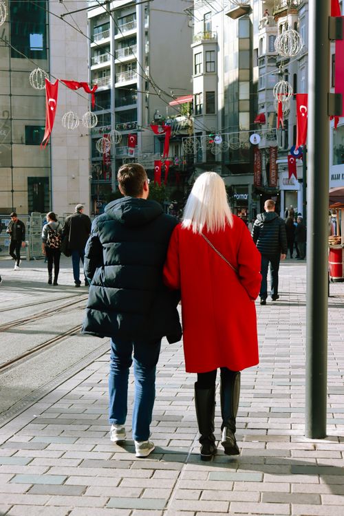 Free A couple walks arm in arm down a bustling city street decorated with flags. Stock Photo