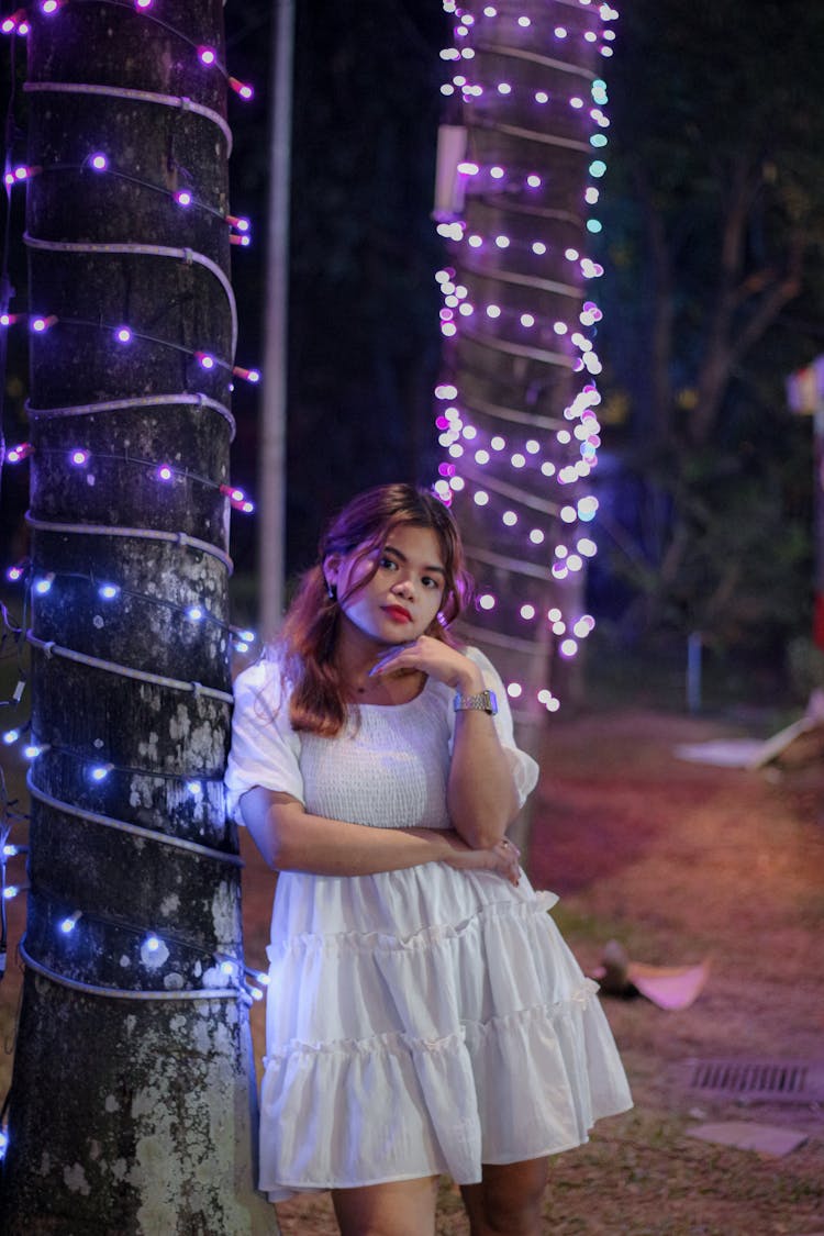 Woman In White Dress Standing Under Tree Decorated With Lights