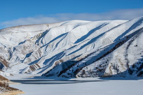 Free Breathtaking view of snow-covered mountains and frozen lake under a clear blue sky. Stock Photo