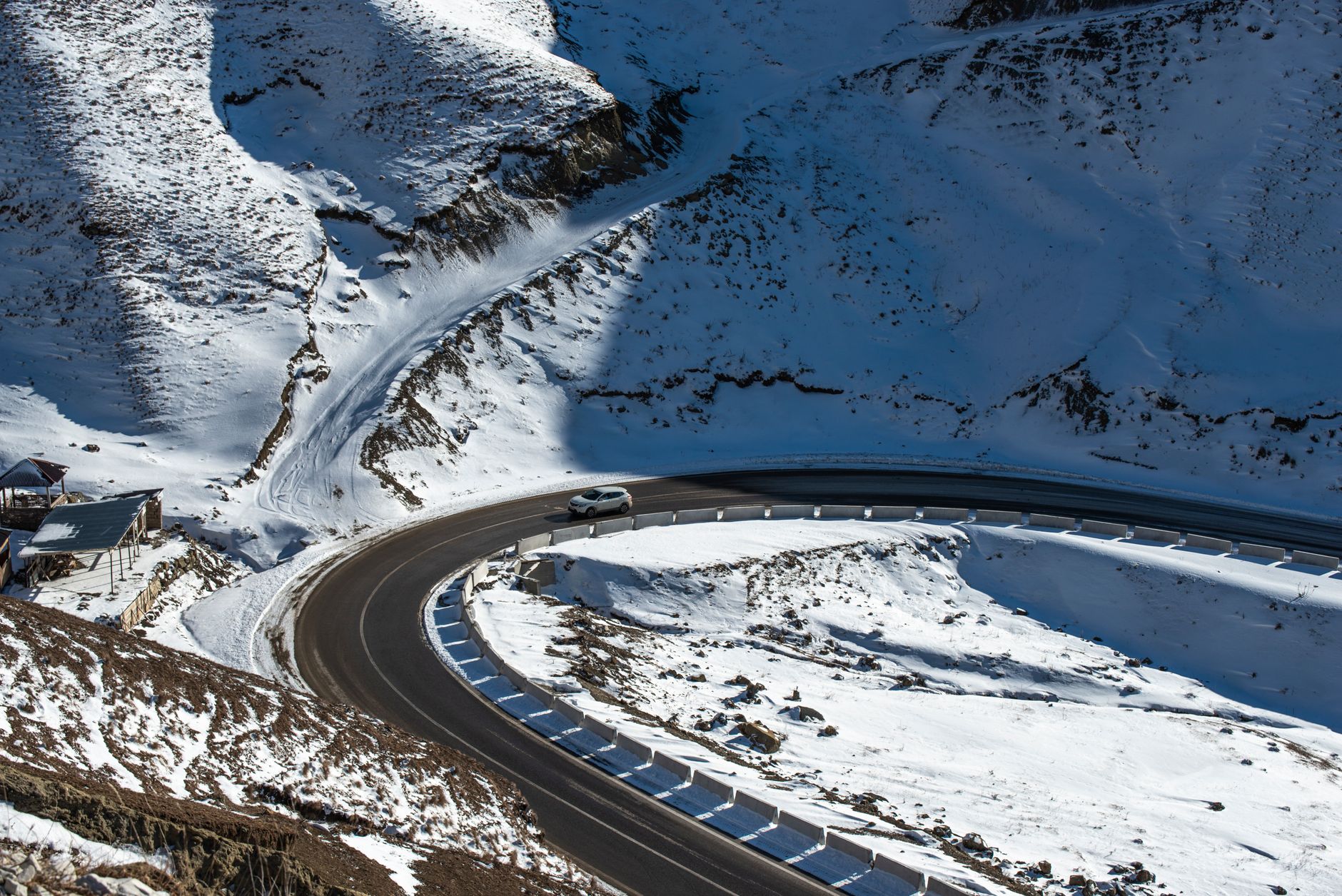 White car navigating a snowy high-altitude switchback on a mountain road