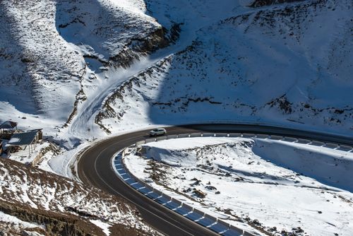 Free A car navigates a scenic winding road through snow-covered mountains in winter. Stock Photo