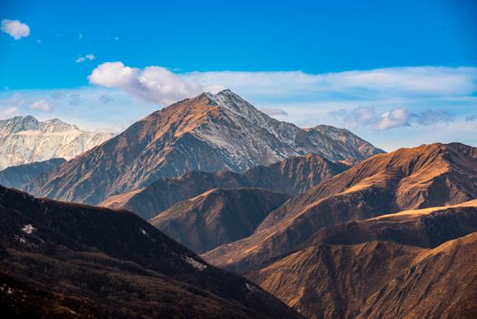 Stunning view of a majestic mountain range with a clear blue sky and clouds.