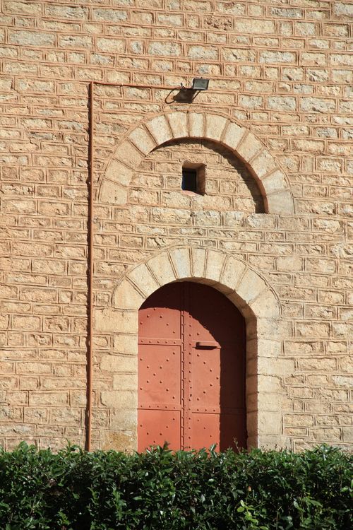 Free Historic stone wall with distinctive arched wooden door and greenery. Stock Photo
