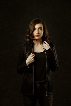 Studio portrait of a woman in a black leather jacket against a dark background, offering copy space.