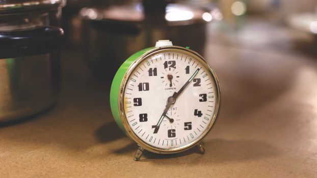 Close-up of a retro alarm clock next to kitchen pots, emphasizing time management in cooking.
