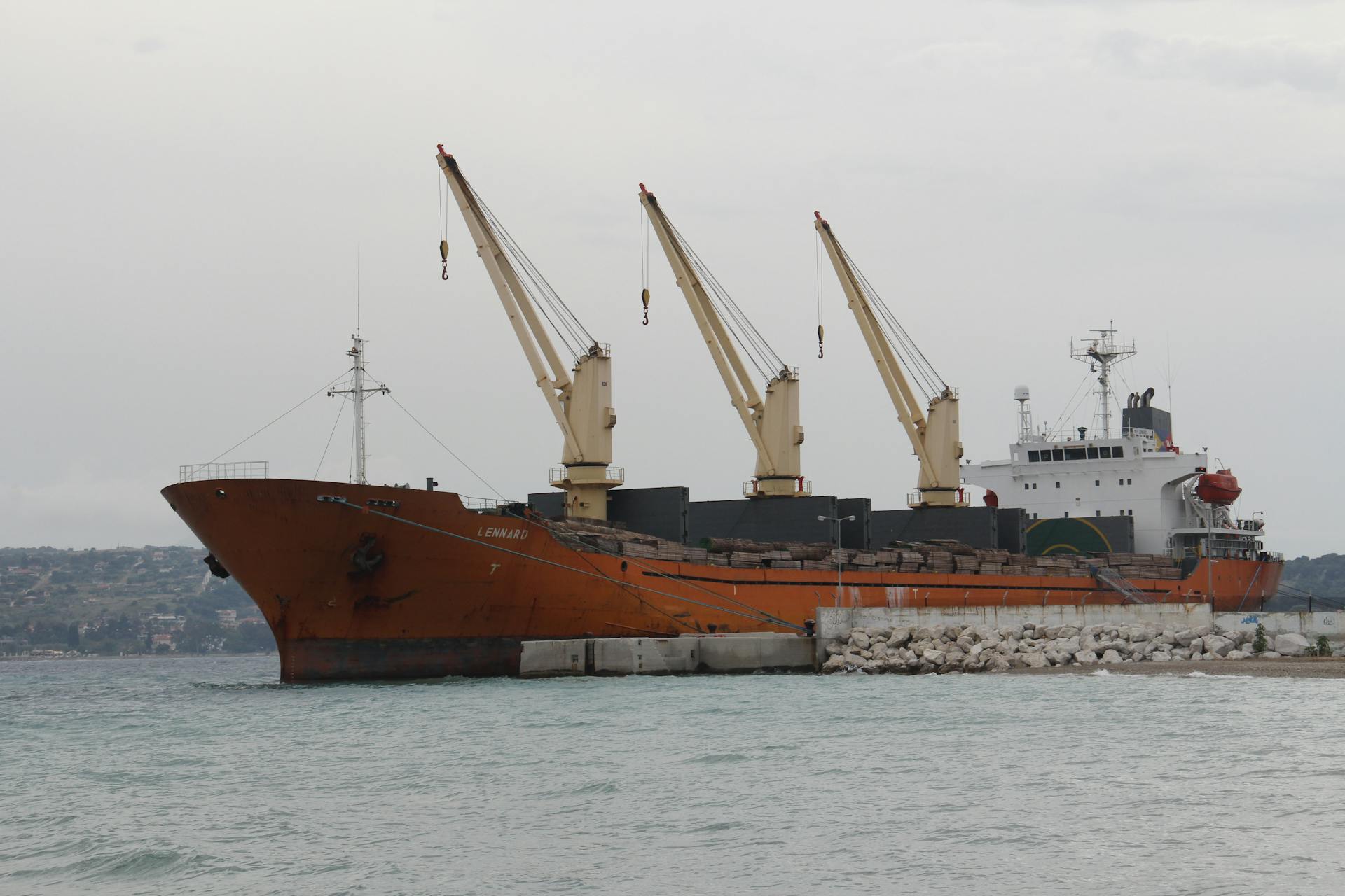 Cargo ship with cranes docked at a port, showcasing maritime logistics.