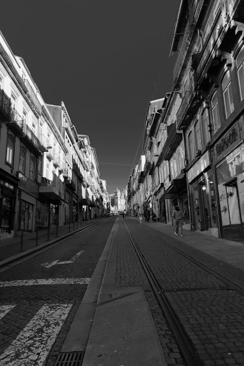 Grayscale Photo of People Walking on the Street Between Buildings 