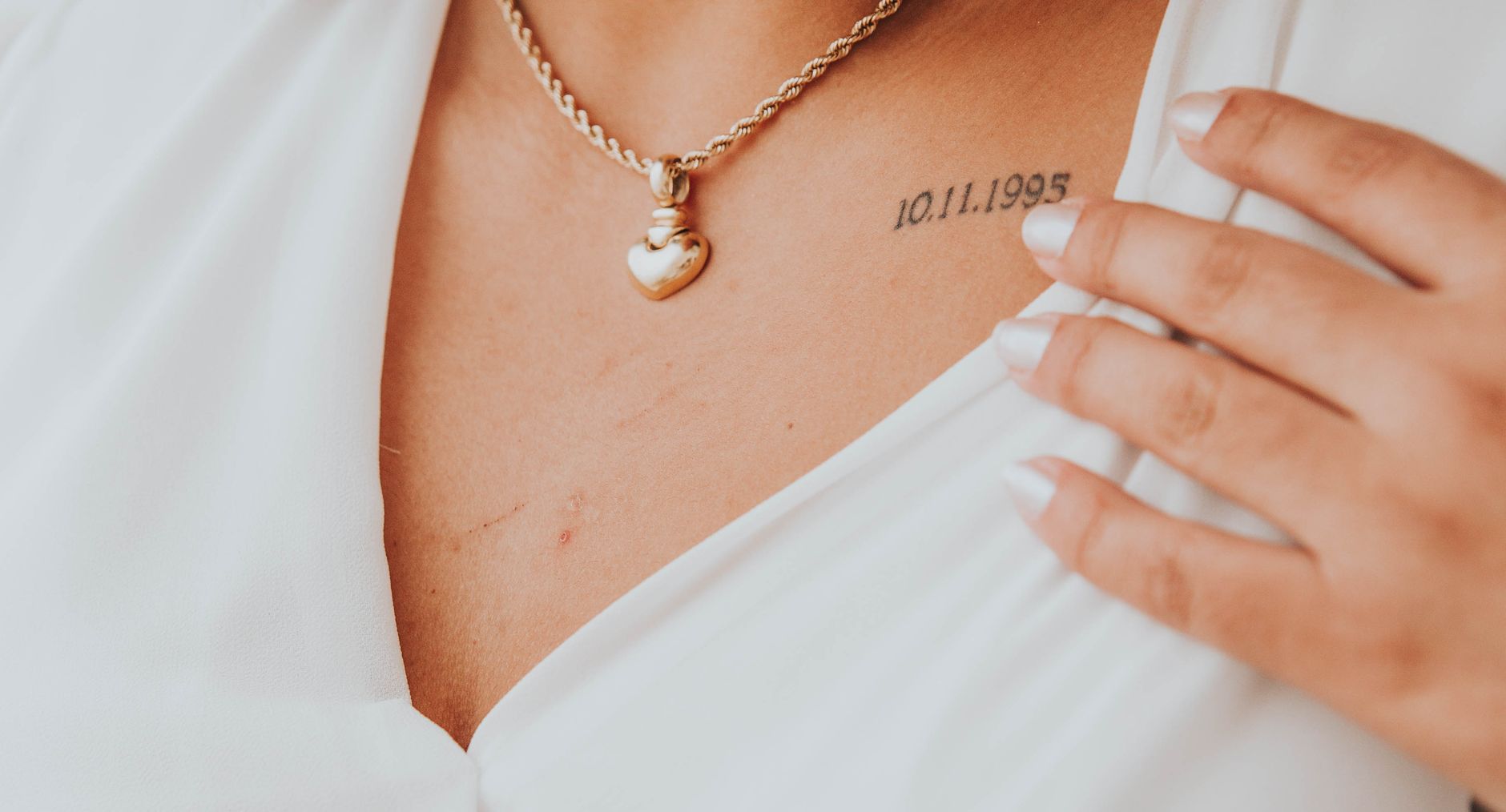 Collier doré porté avec un tatouage éphémère fin sur le décolleté, pour un look bijou de peau