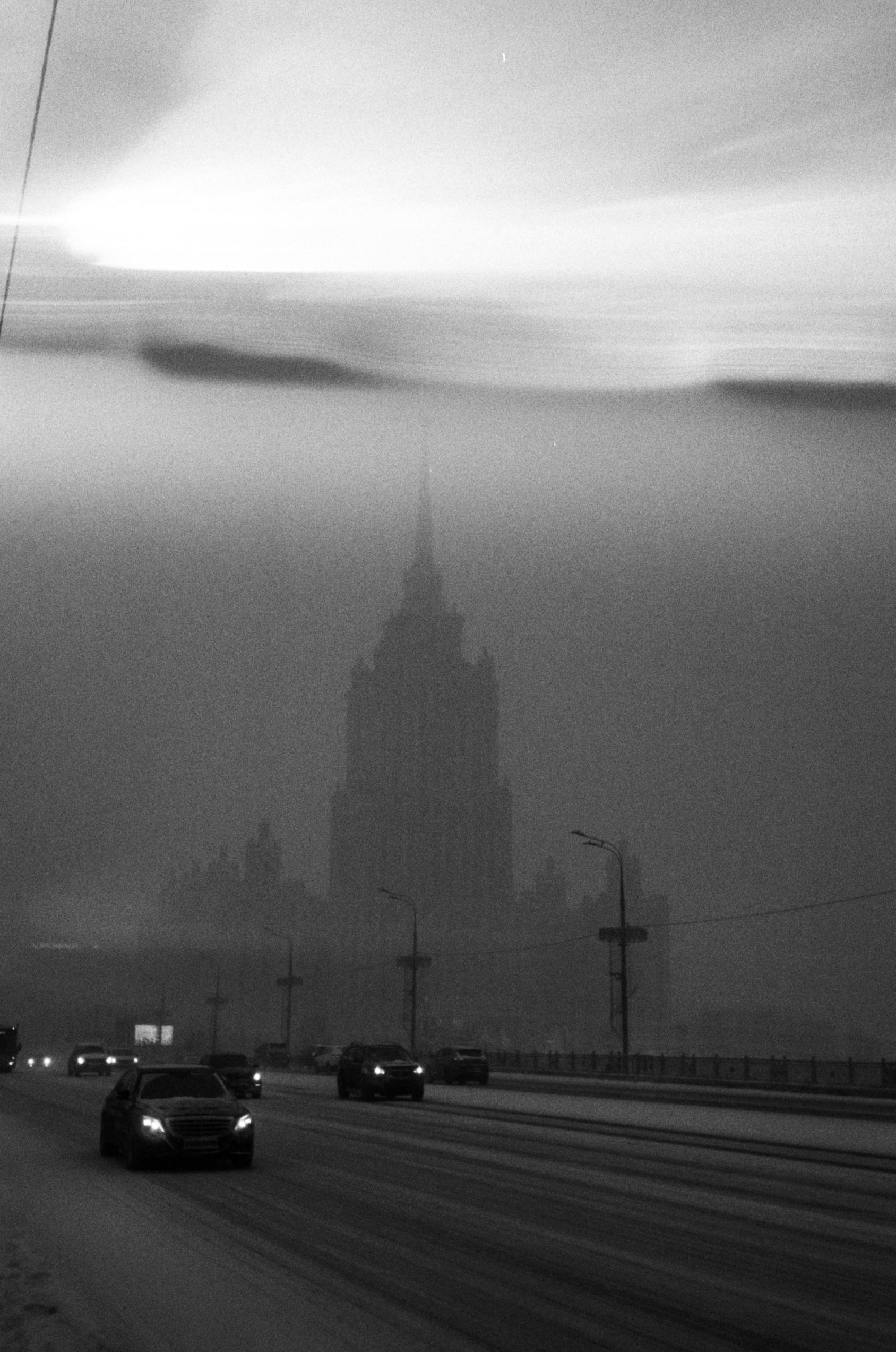 Captivating black and white shot of Moscow street at night, featuring a silhouetted building in fog.