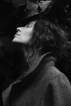 A monochrome close-up portrait of a woman in a coat with eyes closed, evoking a serene mood.