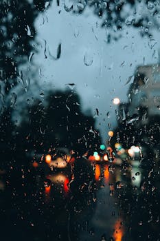 Raindrops on a window with blurred urban lights, capturing a moody evening in Turkey.