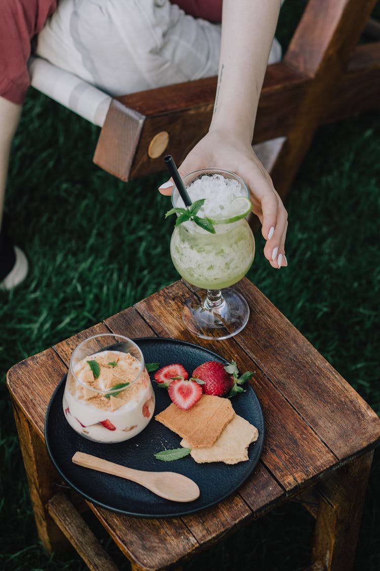 Hand Reaching For Cocktail Standing On Wooden Table