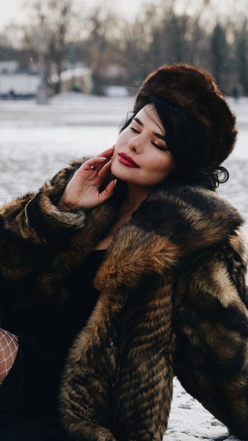 Free Woman in a fur coat savoring the winter outdoors, eyes closed and serene. Stock Photo
