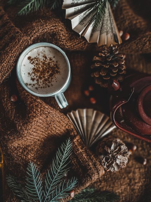 Warm and inviting coffee scene with a mug, pine cones, and a cozy sweater, perfect for winter.