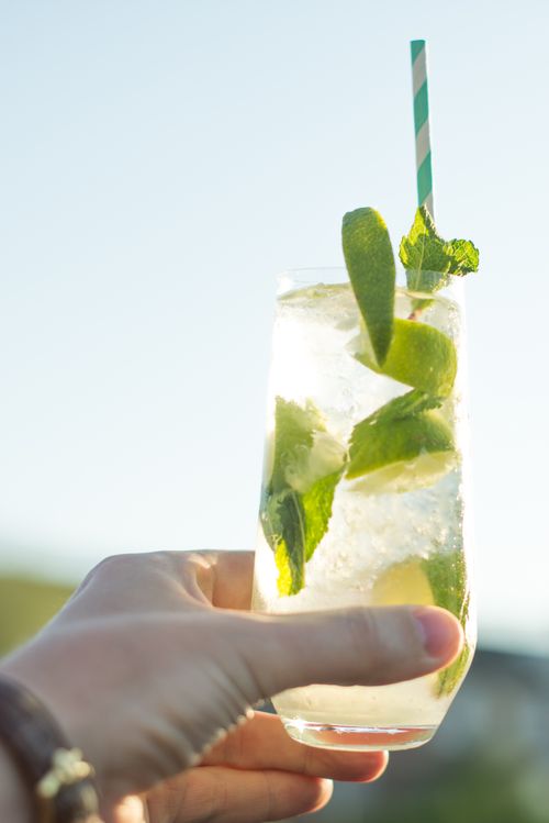 Free Close-up of a refreshing mojito drink with lime slices, mint leaves, and a straw outdoors in bright daylight. Stock Photo