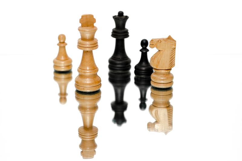 Strategic chess pieces reflecting on a glossy surface, emphasizing strategy and challenge.