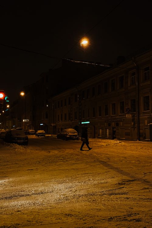 Free A person crosses a snowy street at night, illuminated by city lights, embodying winter's chill. Stock Photo