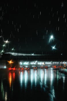 Urban street at night with rain and car lights reflecting on wet pavement.