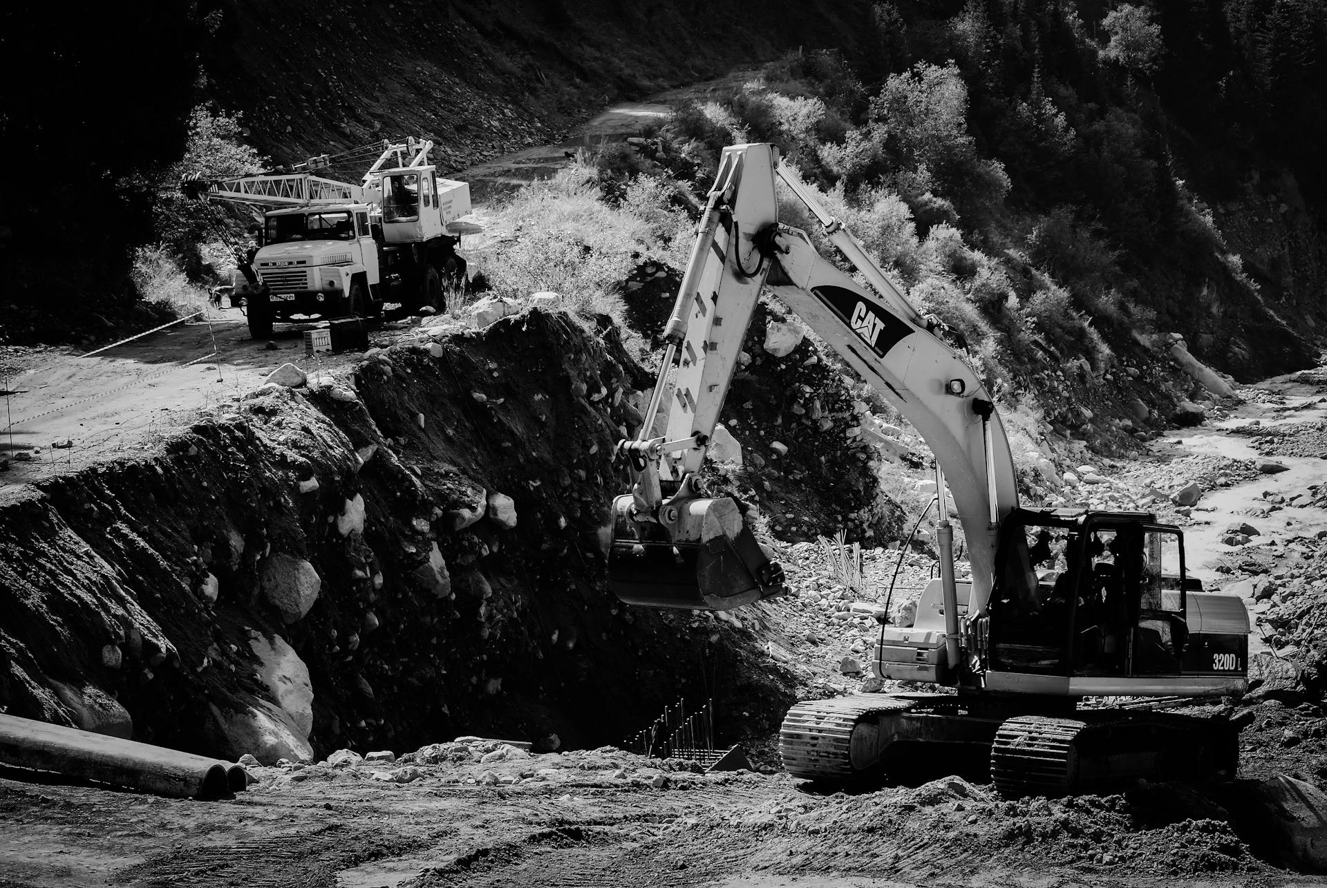 Black and white image of an excavator and truck working in a quarry, highlighting industrial machinery and excavation.