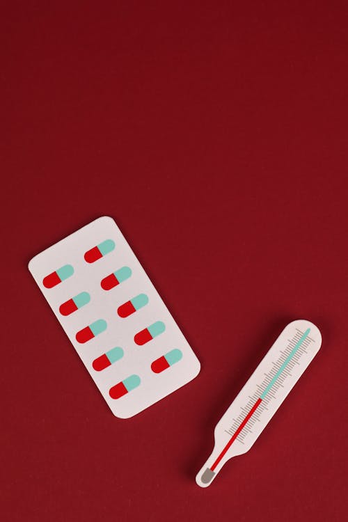 Free A Thermometer and and a Blister Pack of Pills on Red Background Stock Photo