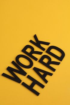 Black letters spelling 'Work Hard' on a bright yellow backdrop for motivation and inspiration.