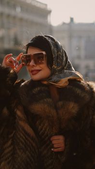 Stylish woman in fur coat smiling with sunglasses outdoors.