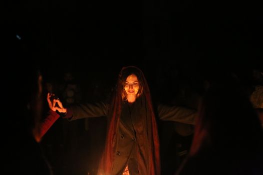 A woman performs a mystical ritual around a fire at night in Italy, surrounded by people.