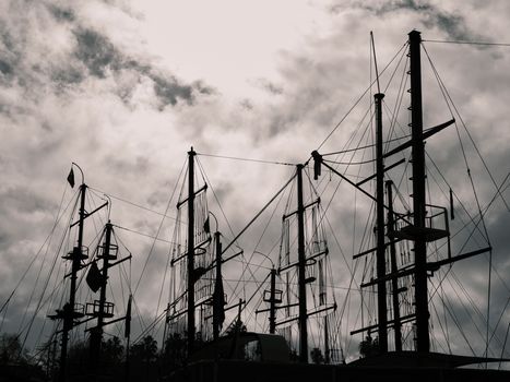 Silhouetted masts of sailboats create a striking contrast against a moody, cloudy sky.