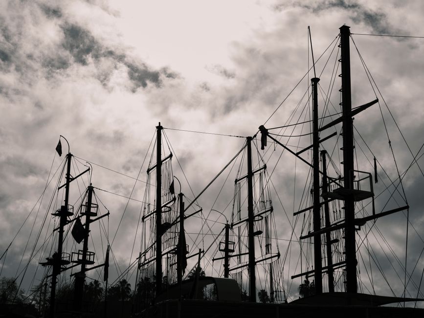 Silhouetted masts of sailboats create a striking contrast against a moody, cloudy sky.