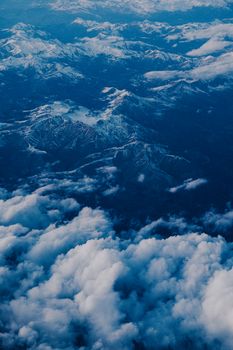 A breathtaking aerial view of rugged snow-capped mountains surrounded by fluffy clouds.