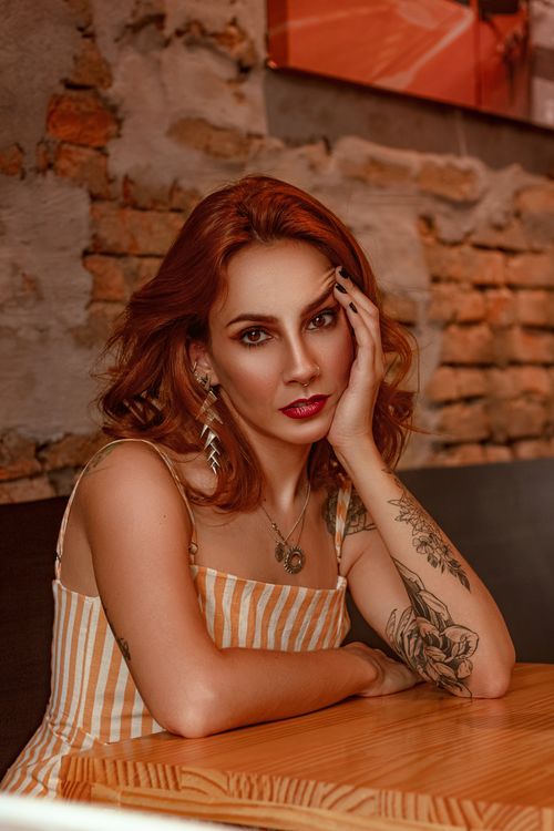 Free Portrait of a woman with tattoos and red hair in a modern indoor setting. Stock Photo