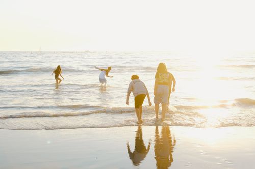 Free People playing in the gentle waves of a sunlit beach, captured during daytime. Stock Photo