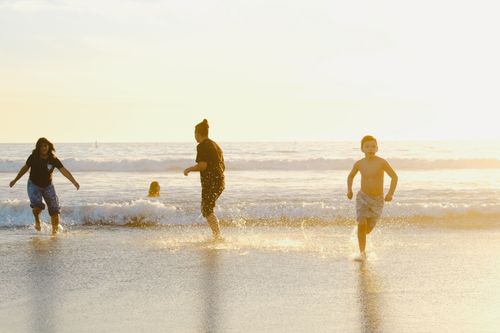 Free Youngsters run and play in the surf during a vibrant sunset at the beach. Stock Photo