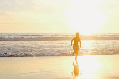 Free A young boy runs along the beach at sunset, casting a silhouette against the golden waves. Stock Photo