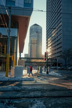A person walking in a cityscape with snow, skyscrapers, and stoplights on a sunny winter day.