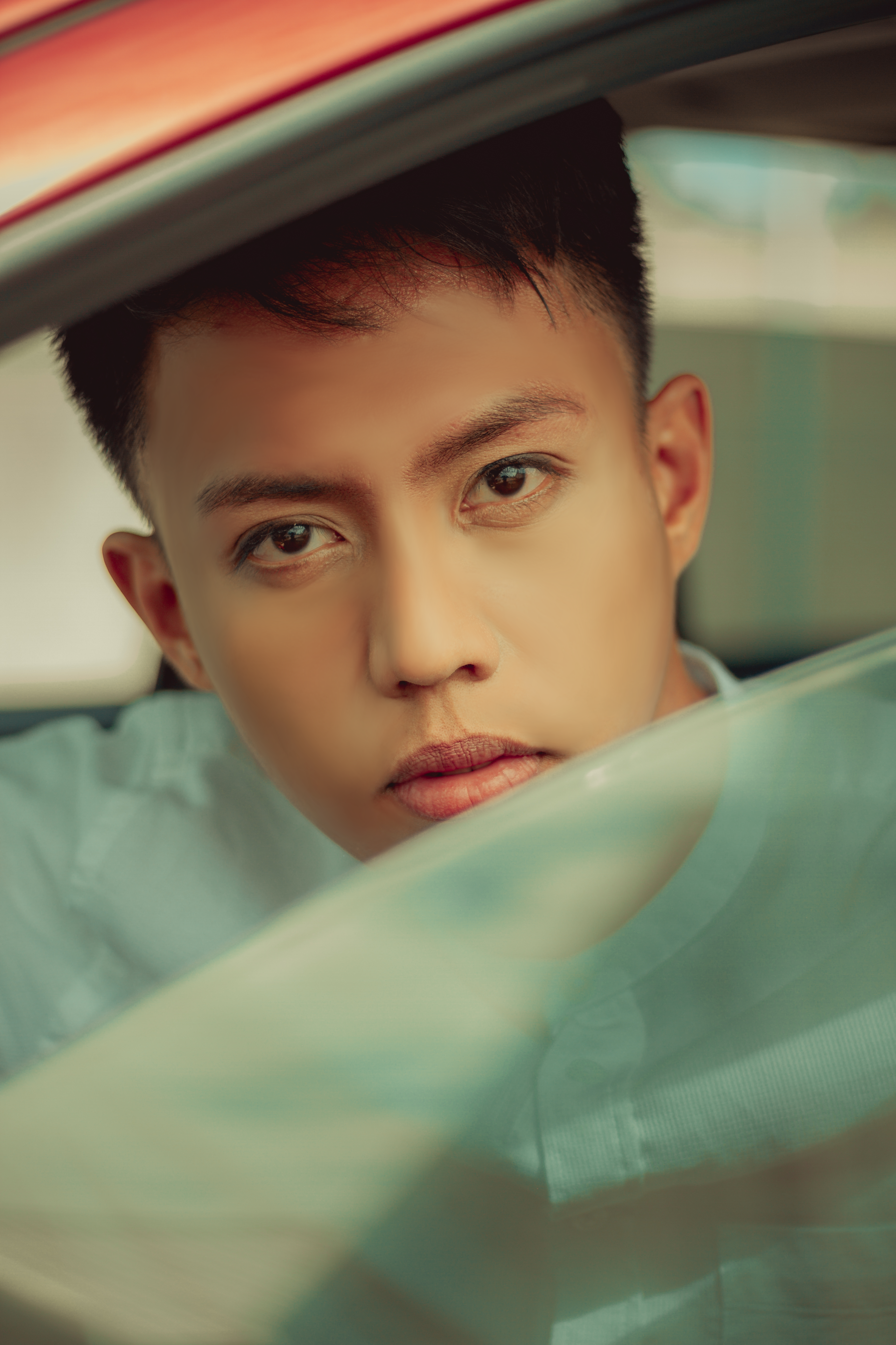 Portrait of a young man sitting inside a car, with a focused, thoughtful expression.