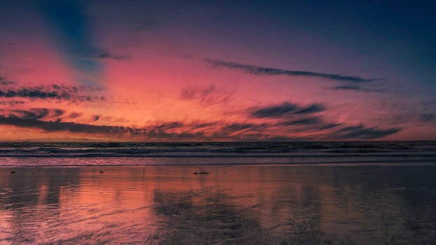 Stunning sunset over the ocean with vibrant colors reflecting on the wet sandy shoreline.