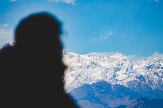 Silhouette of a person with snow-covered mountains and blue sky in the background.