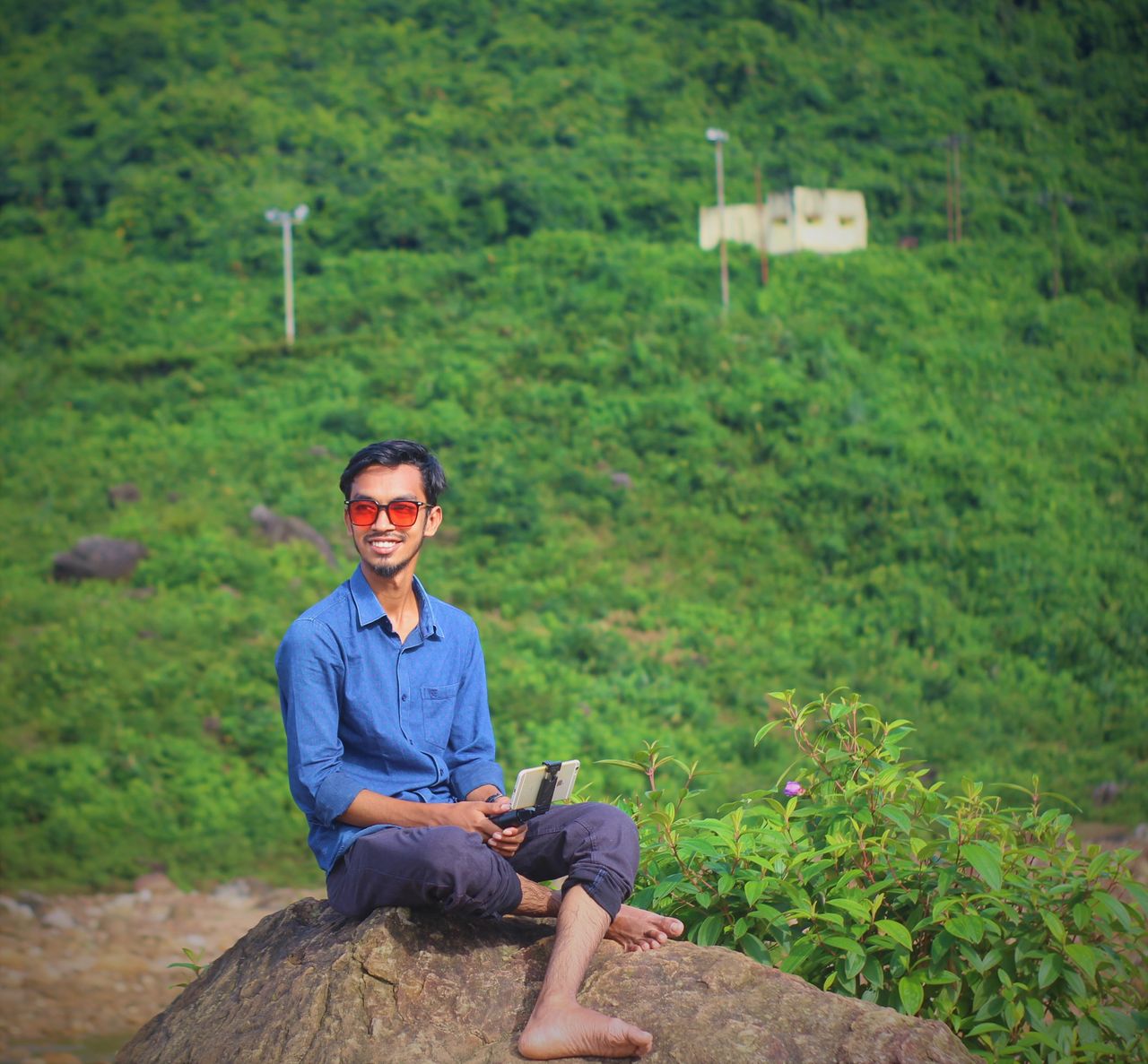 a young man sitting on a rock enjoying a lush green hill view smiling