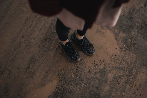 A Person Wearing Black Sneakers on Dirt Road