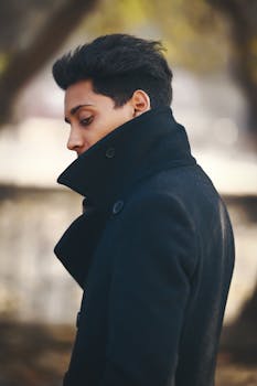 Side profile of a man in a black coat outdoors with a contemplative pose.